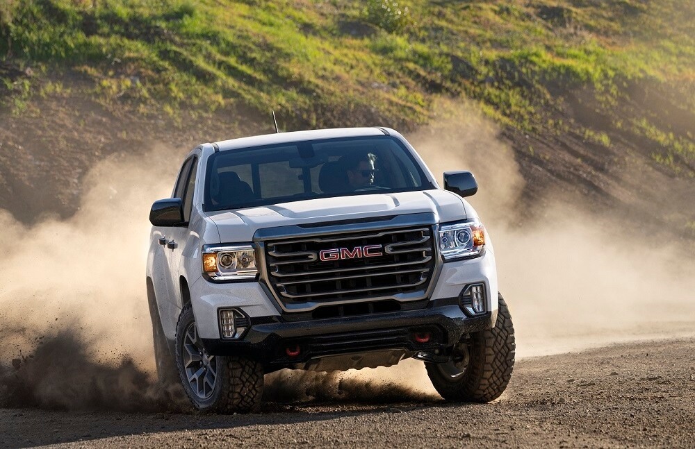 A white GMC truck driving through gravel and sand.
