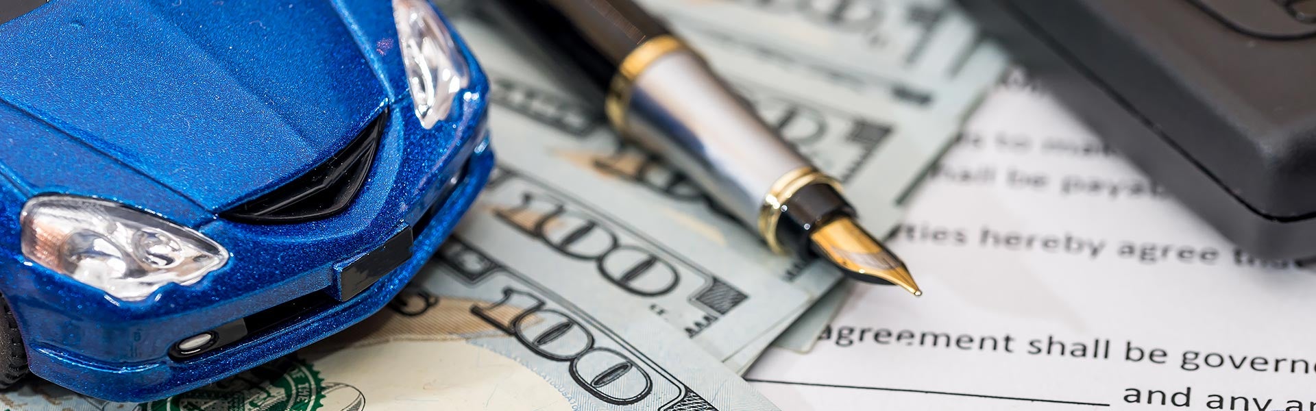 A small model car sitting on top of money with a pen and form next to it.